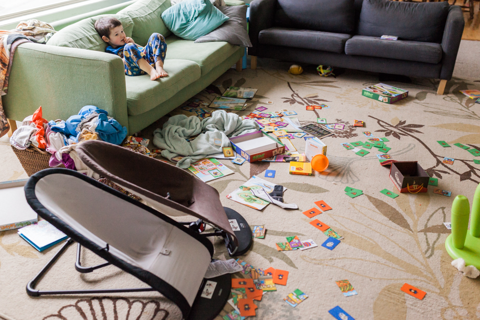 Little boy sits on couch in cluttered room - Family Documentary Photography