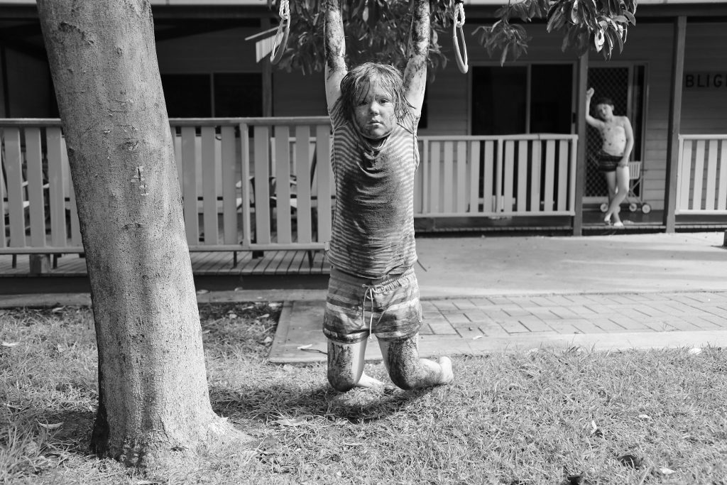 muddy girl hangs on tree limb