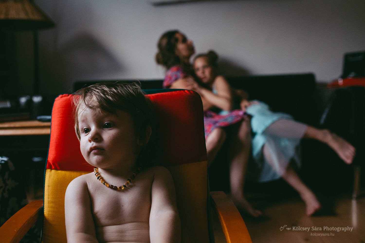 Child sits in dramatic light with family cuddling behind - Family Documentary Favorite