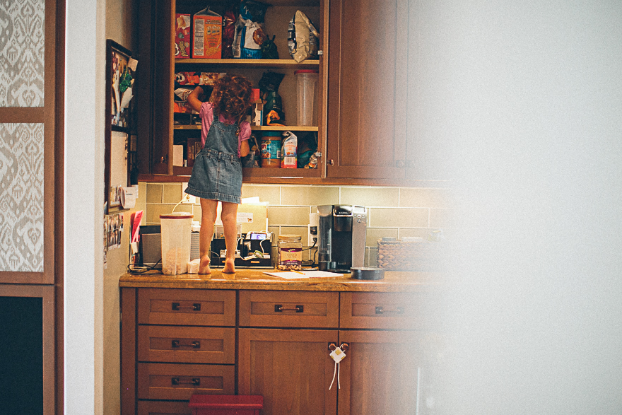 girl standing on counter looking in cabinets - family documentary photography