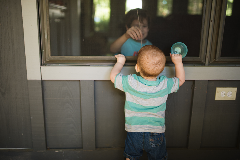 baby looks at boy through window - Family Documentary Photography