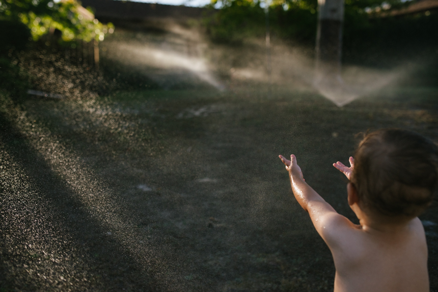 child reaching toward sprinklers - Family Documentary Photography