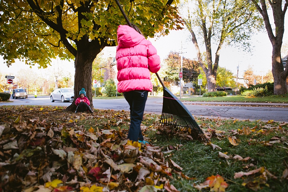 girl in pink coat rakes leaves - Family Documentary Photography