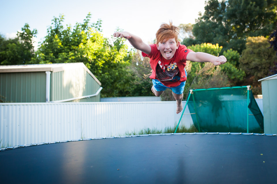 boy in superhero pose on trampoline - Family Documentary Photography