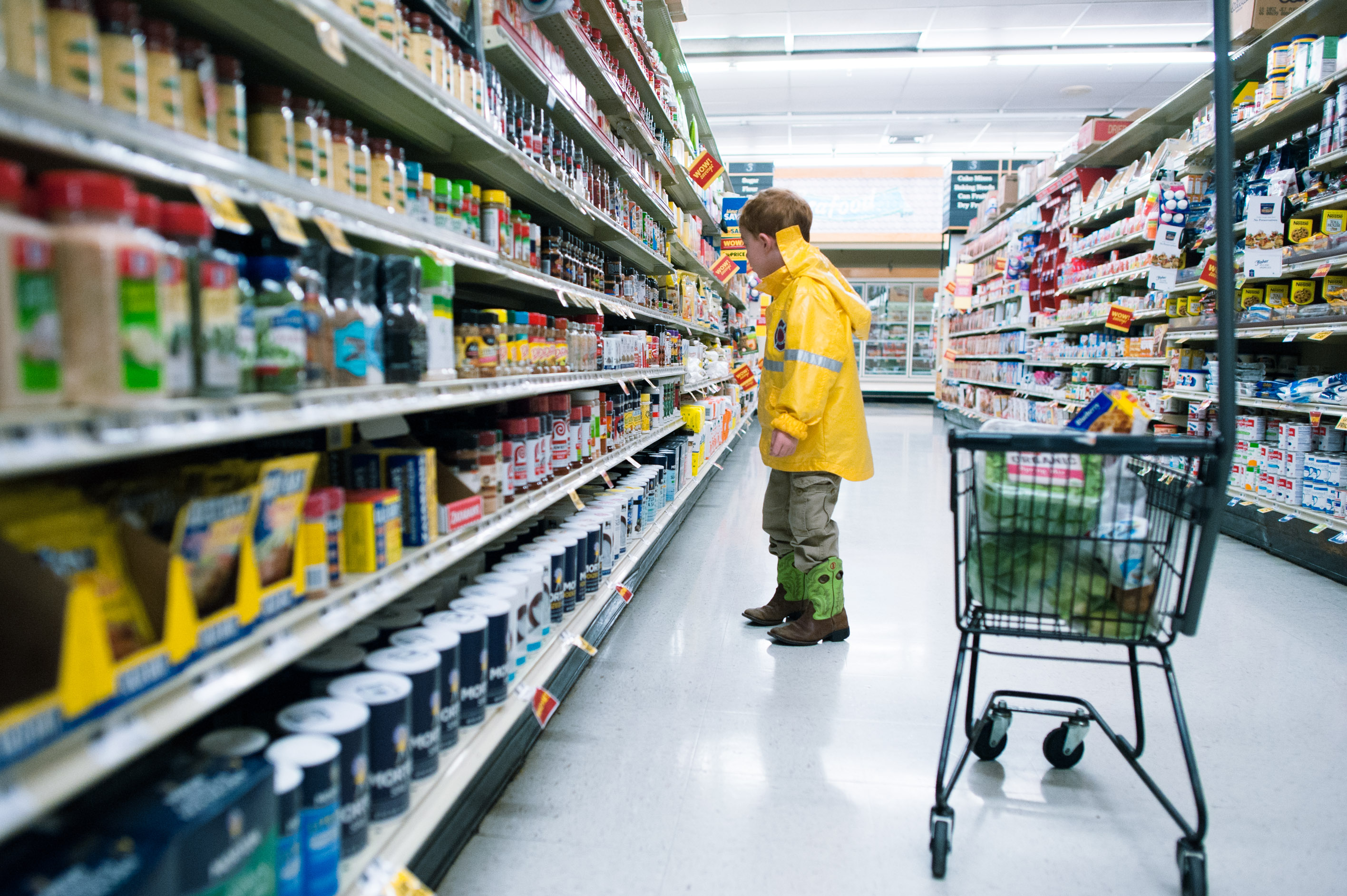 boy wearing bright yellow jacket looking at supermarket shelf