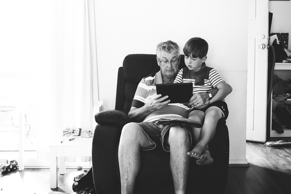 Older man looks at tablet with boy in his lap - Family Documentary Photography