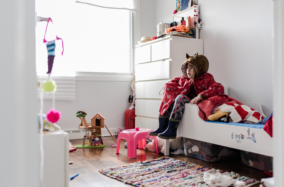 girl sits on bed wrapped in blankets wearing hood with ears - Family Documentary Photography