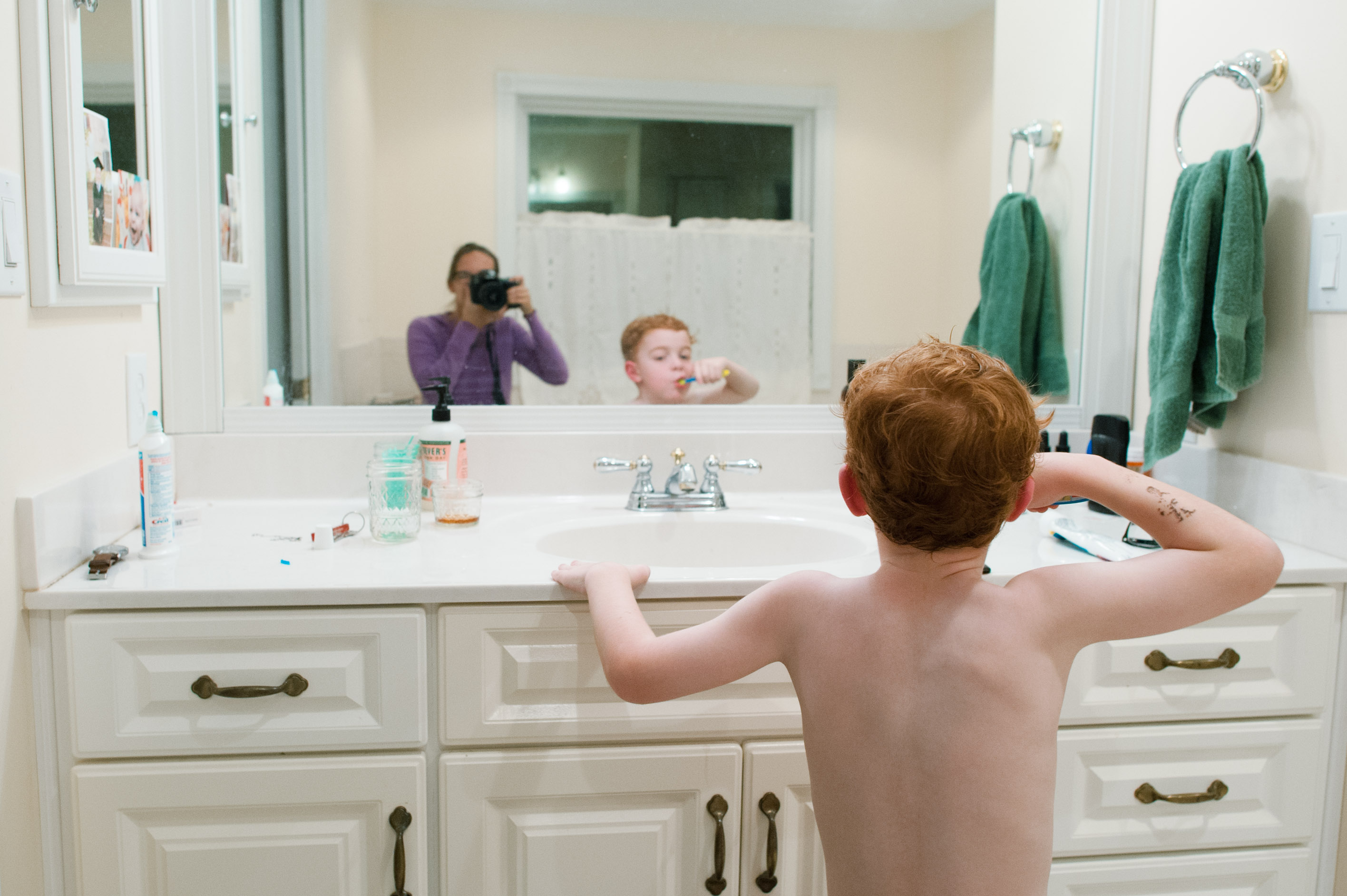 Self portrait of mother in bathroom mirror while son brushes teeth