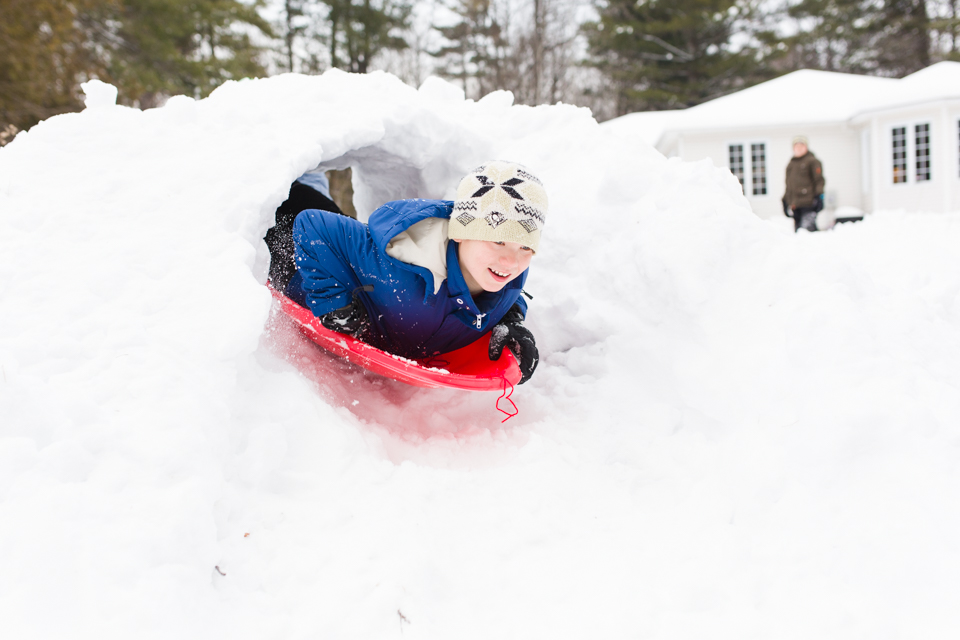 boy sledding through snow tunnel -Documentary Family Photography