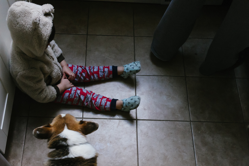 Boy in coat pout with dog on kitchen floor - Documentary Family Photography