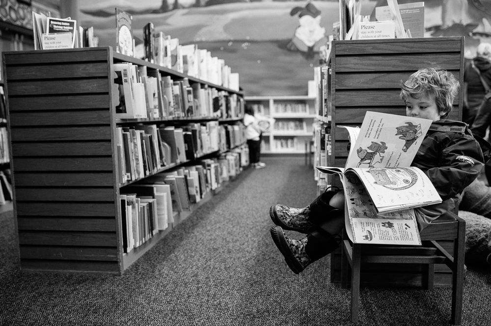 boy looks at picture book in library - Documentary Family Photography