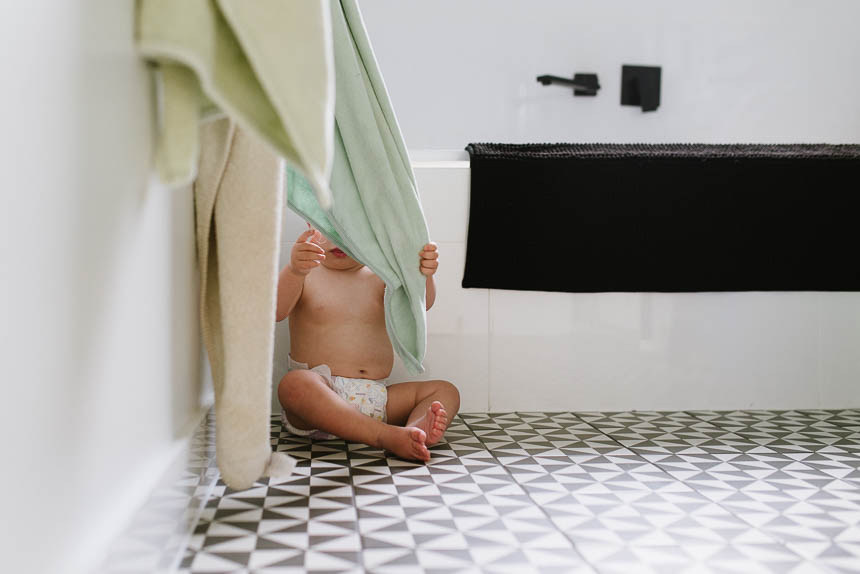 baby hides behind bath towel - Documentary Family Photography