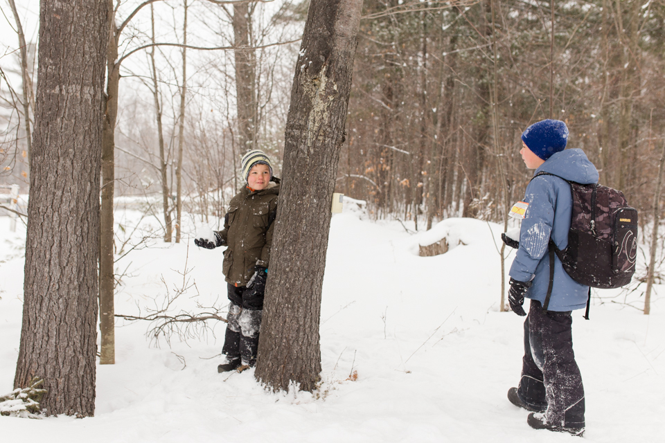 boy waiting behind tree with snowball - Documentary Family Photography