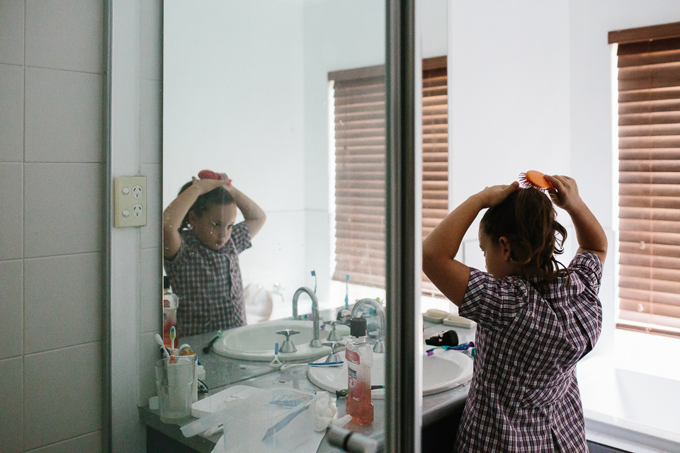 girl brushing hair in bathroom mirror - Documentary Family Photography