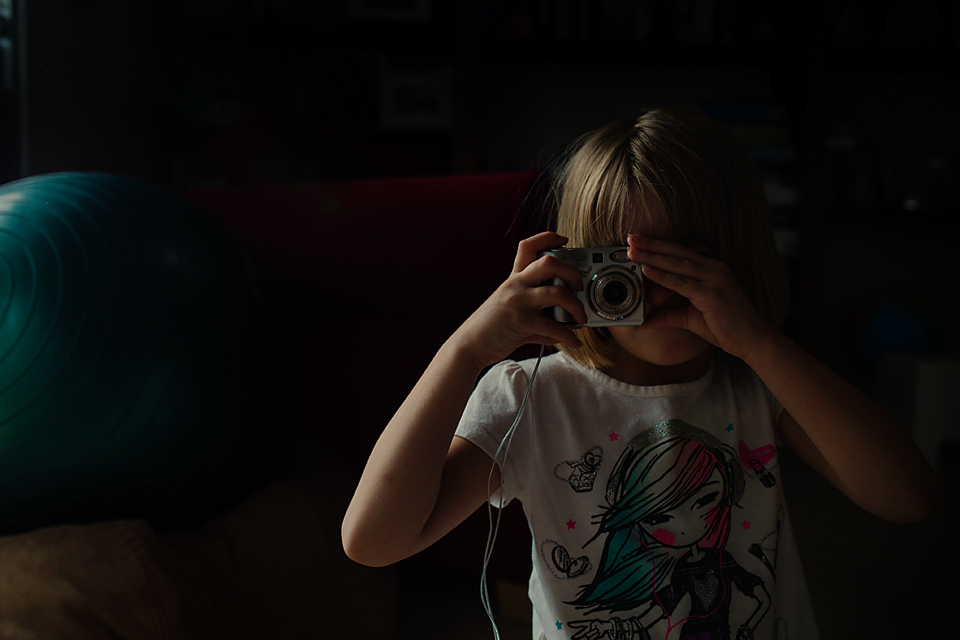 girl using little camera in moody light - Documentary Family Photography
