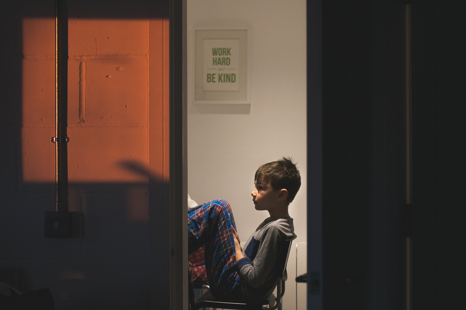 boy leaning back in chair as seen through door frame - Documentary Family Photography