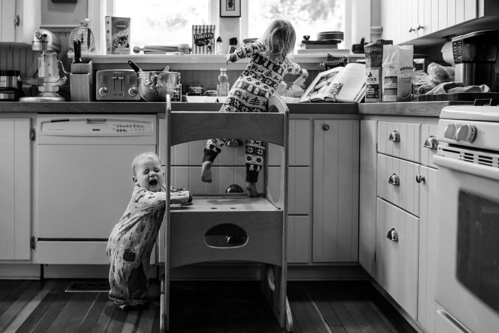 child at kitchen sink while baby cries at feet - Documentary Family Photography