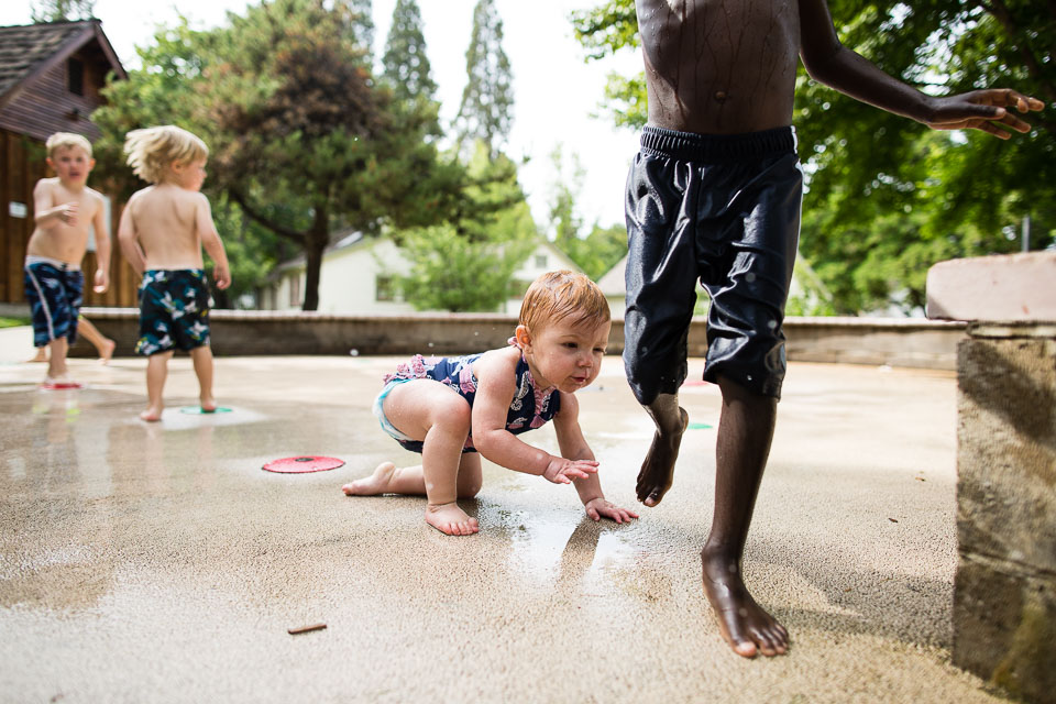 baby crawling after boy in splash pad