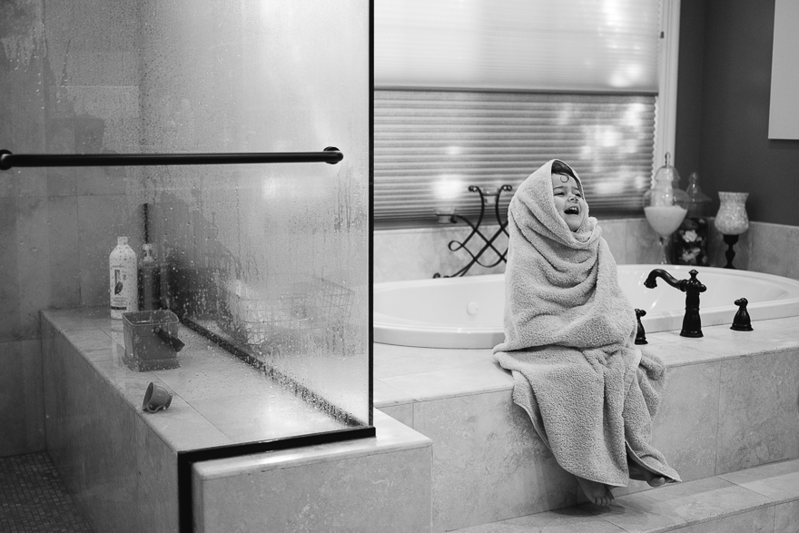 girl wrapped in towel sitting on tub edge - documentary family photography