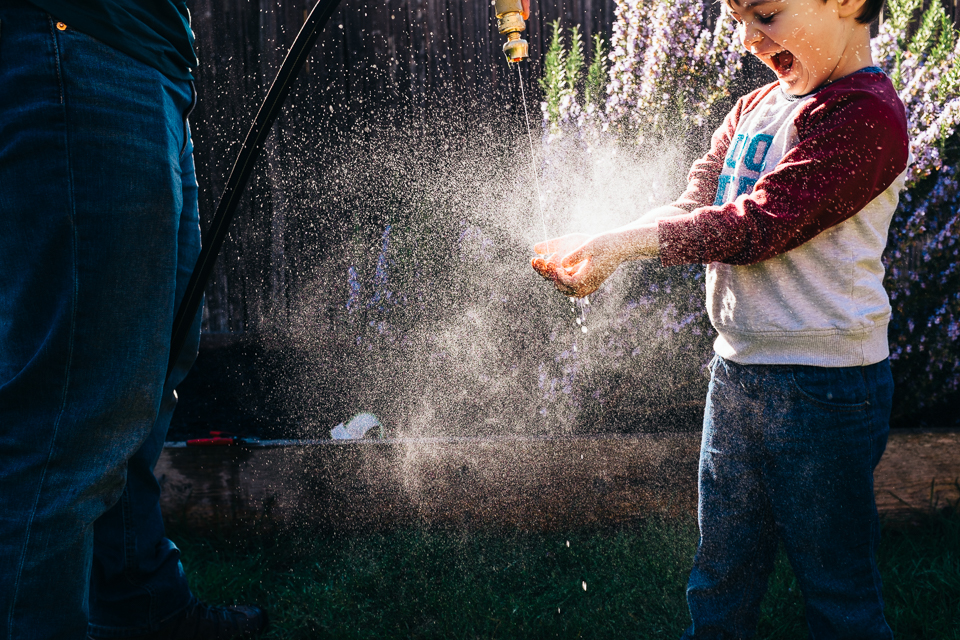 boy has hands washed in garden hose - Documentary Family Photography
