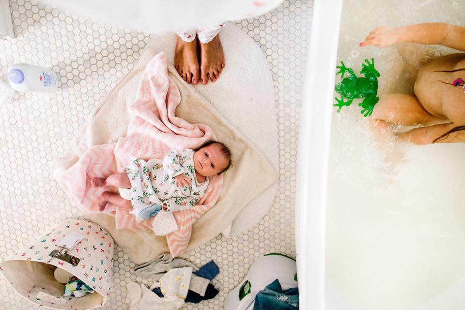 baby on floor while child is in bath - Documentary Family Photography