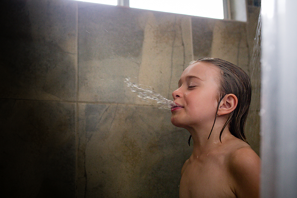 girl spitting out water in shower - Documentary Family Photography