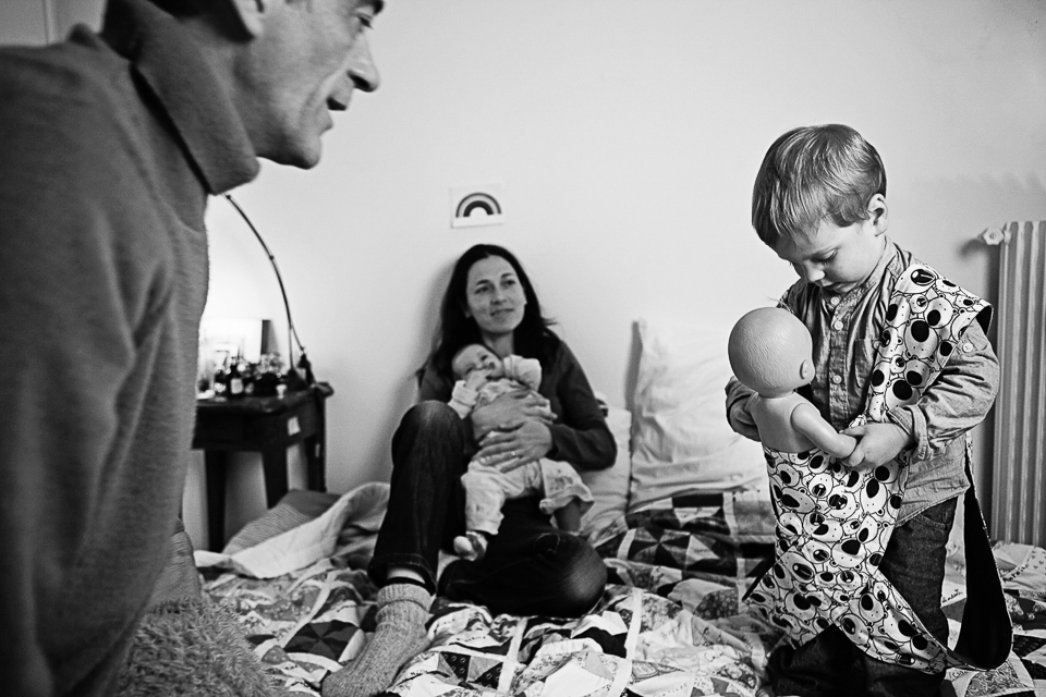 family on bed while child puts doll in carrier - documentary family photography