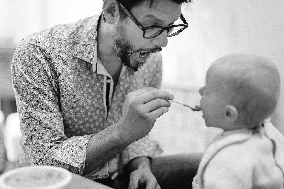 father makes face while he feeds baby - documentary family photography