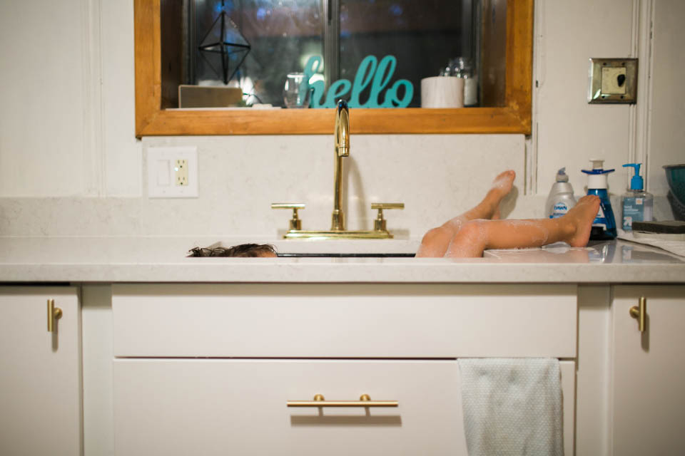 girl lounging in kitchen sink - Documentary Family Photography
