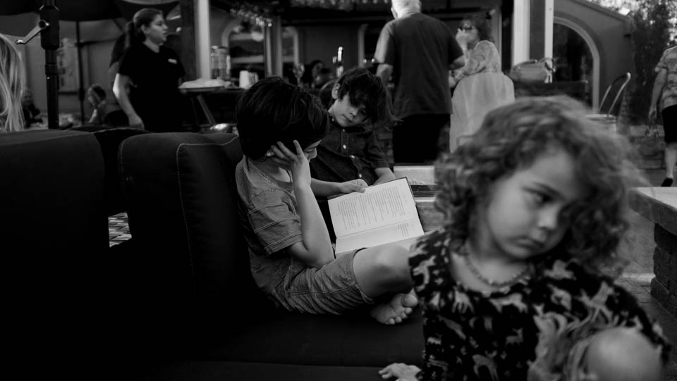 boy reads while girl is bored - Documentary Family Photography