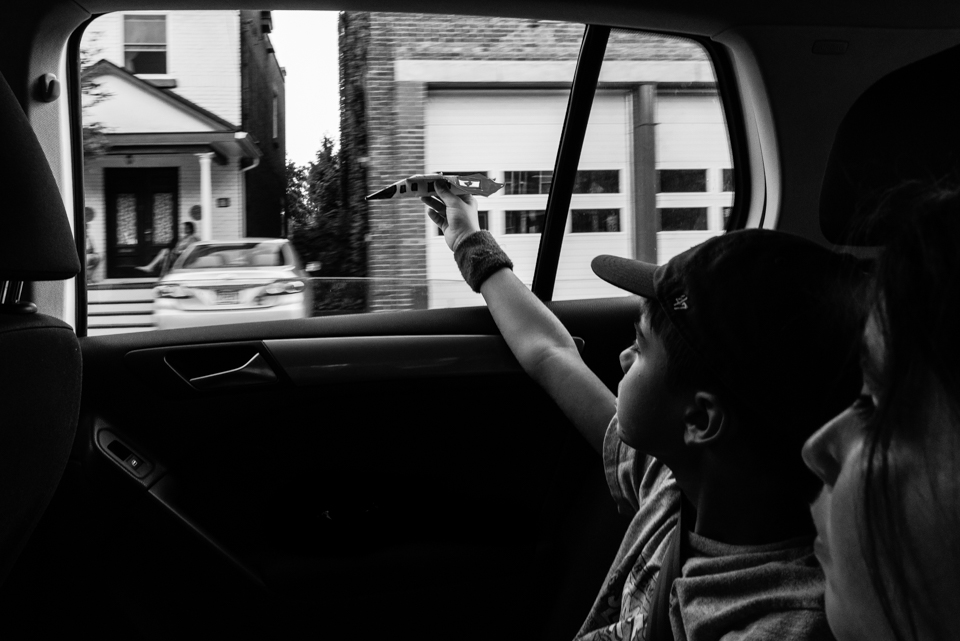 child flies toy plane out car window - Documentary Family Photography