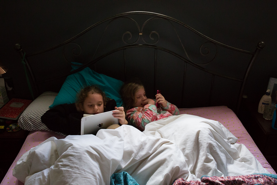 girls on tablet in bed - Documentary Family Photogarphy
