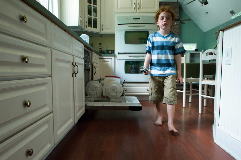 Boy walks through kitchen making sour face - Documentary Family Photogarphy