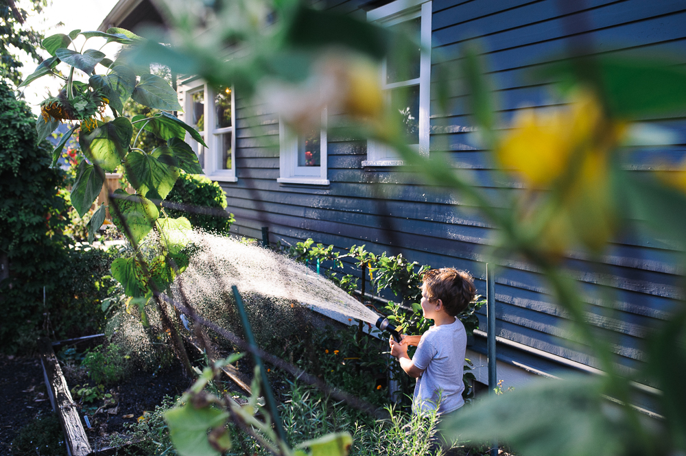 boy sprays water from hose - Documentary Family Photography