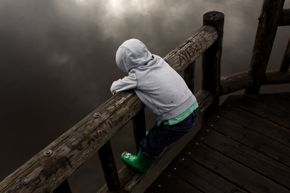 boy stands on bridge and gazes at water - Documentary Family Photography