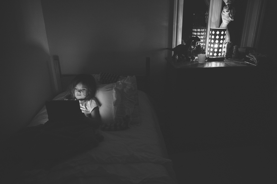 girl working on laptop in dark room - Documentary Family Photography