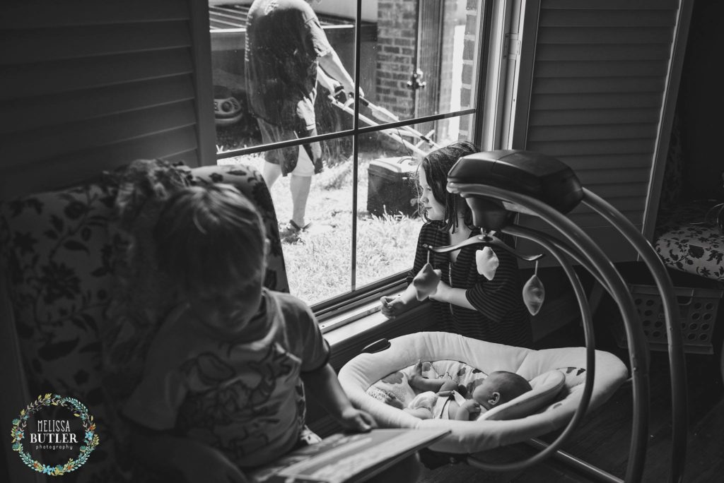 baby watches man mow lawn out window - Documentary Family Photography