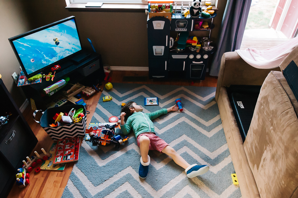 boy sprawls on floor amidst toys - Documentary Family Photography