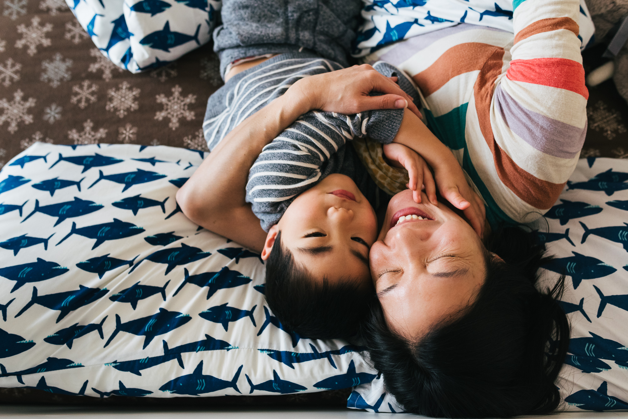 mother snuggles with son on bed