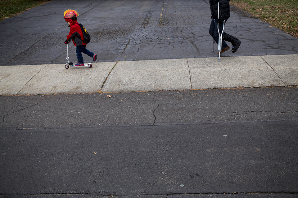 kid on scooter followed by parent on crutches