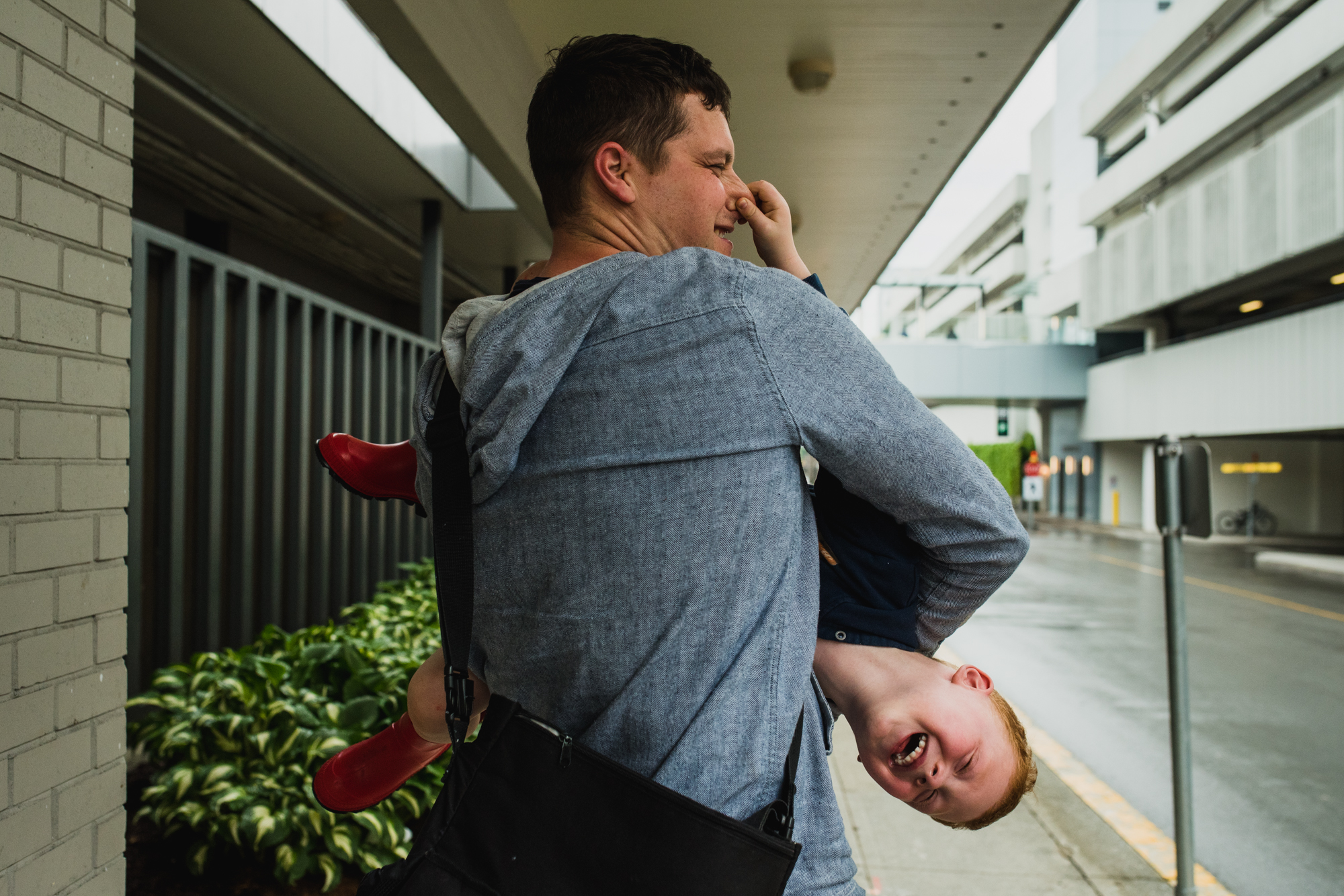 Dad carrying a boy sideways who is trying to pinch his nose