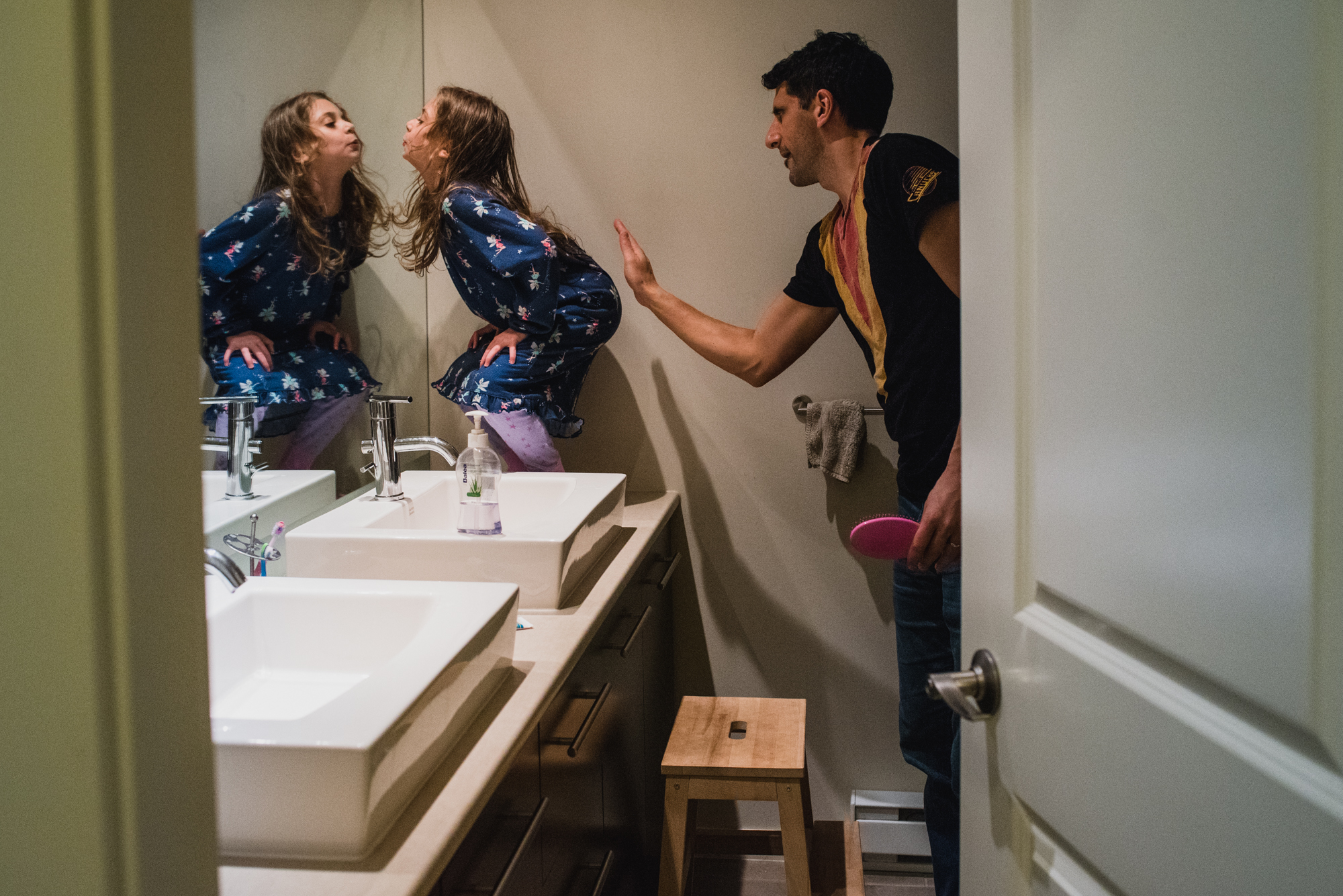 Dad trying to stop the silliness of his daughter in front of the mirror