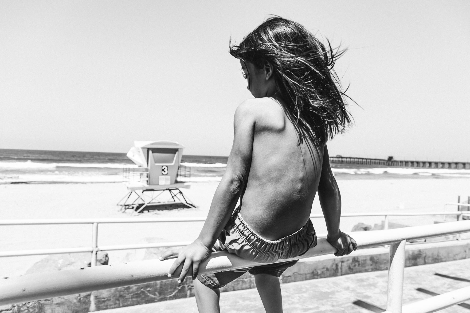 child sitting on rail at beach