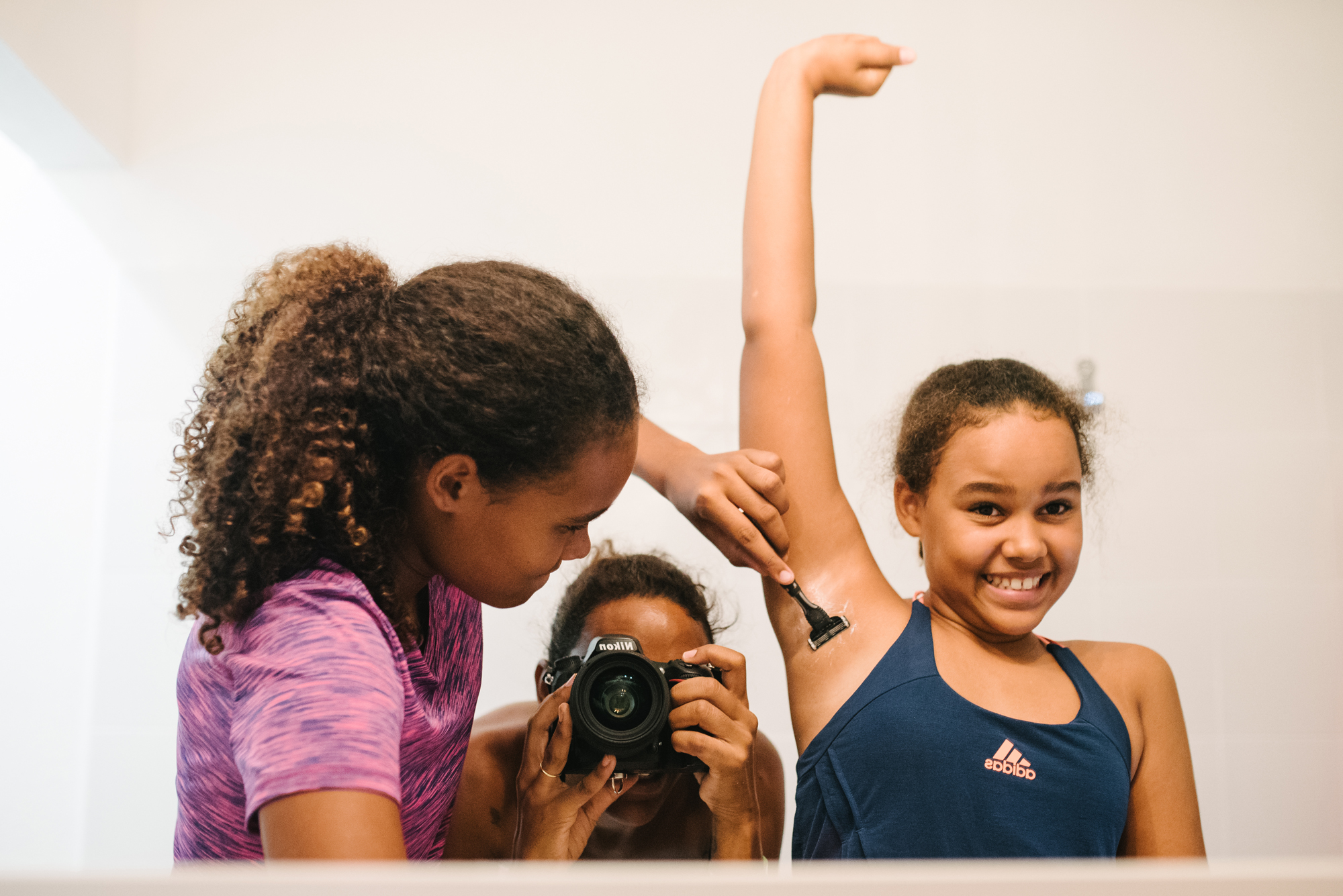sister teaches younger how to shave underarms - Documentary Family Photography