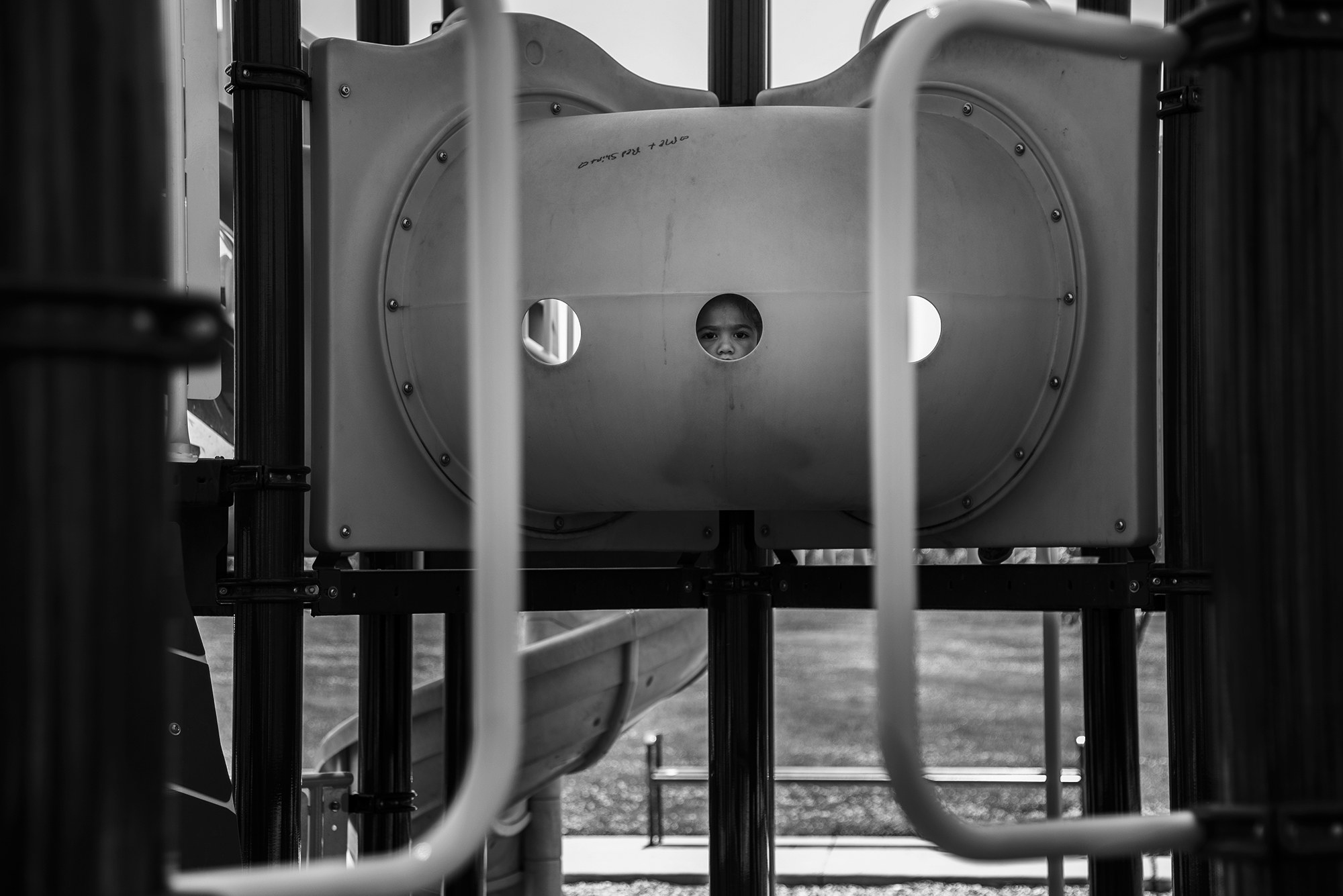 kid peering through playground equipment - Documentary family photography