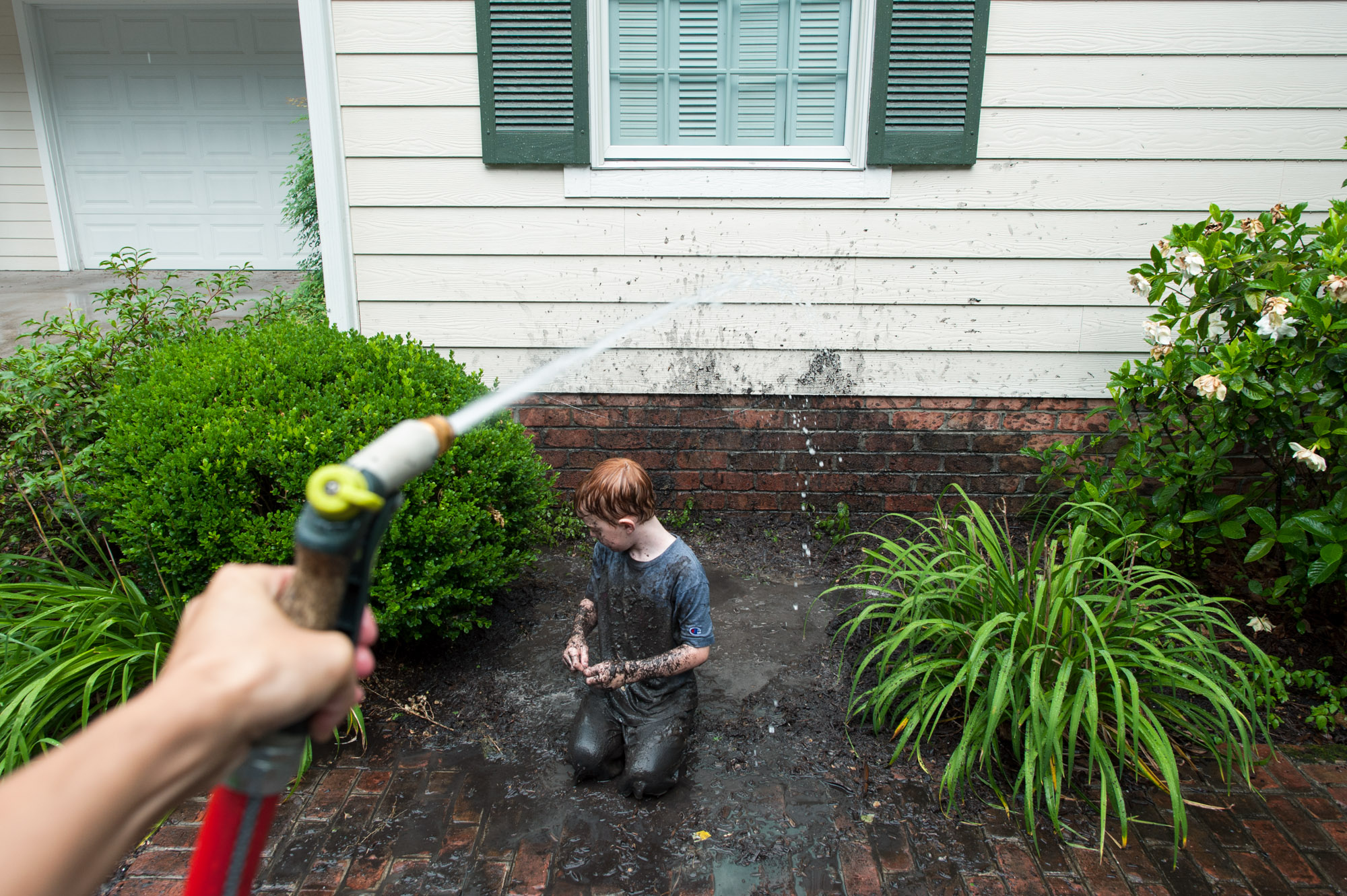 boy in mud being cleaned with hose - Documentary family photography