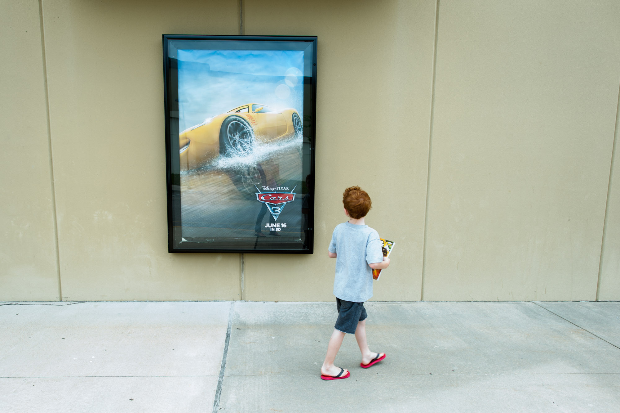 boy walks past movie poster - Documentary Family Photography