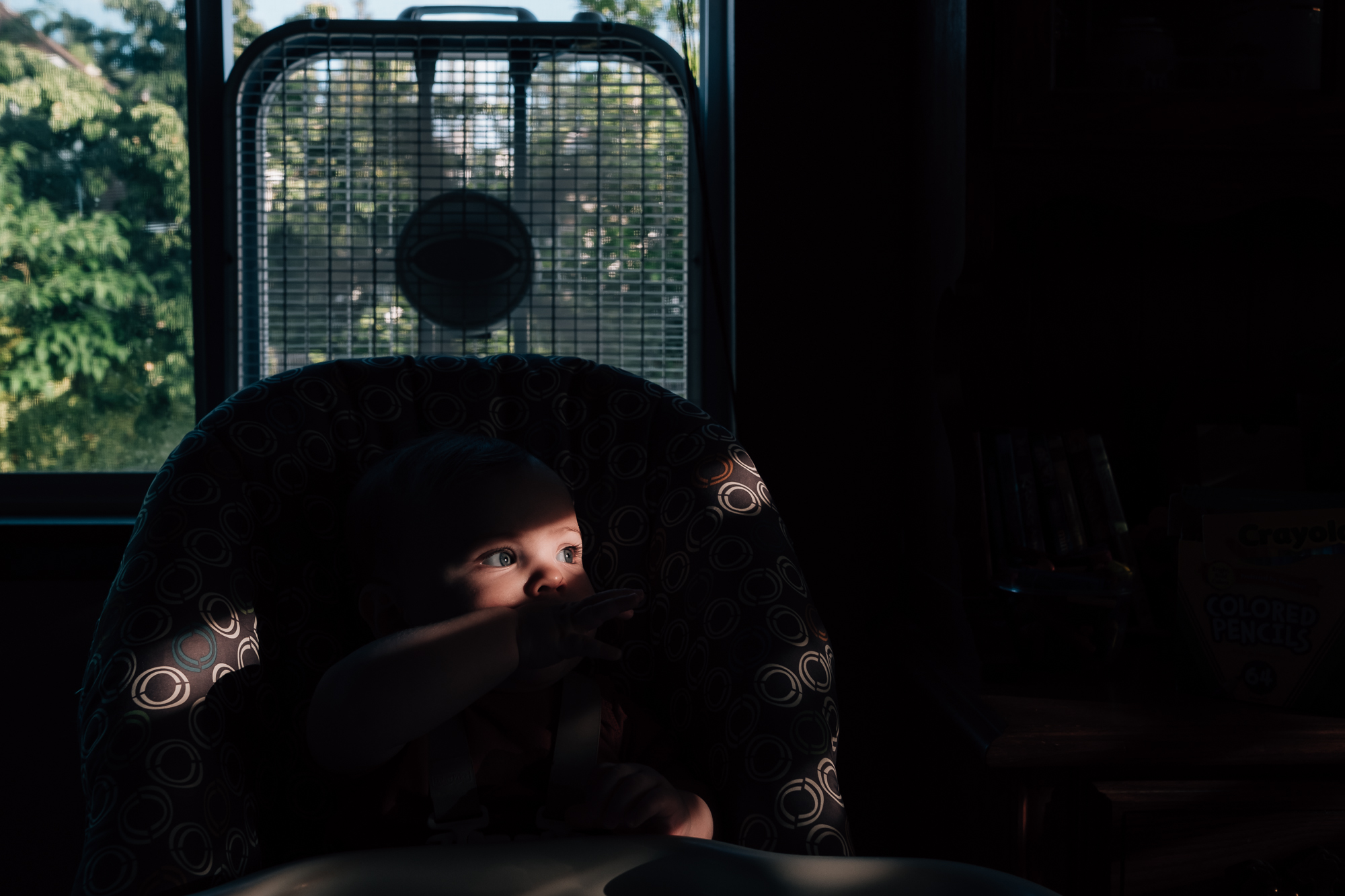 baby in high chair with shaft of light - Documentary Family Photography