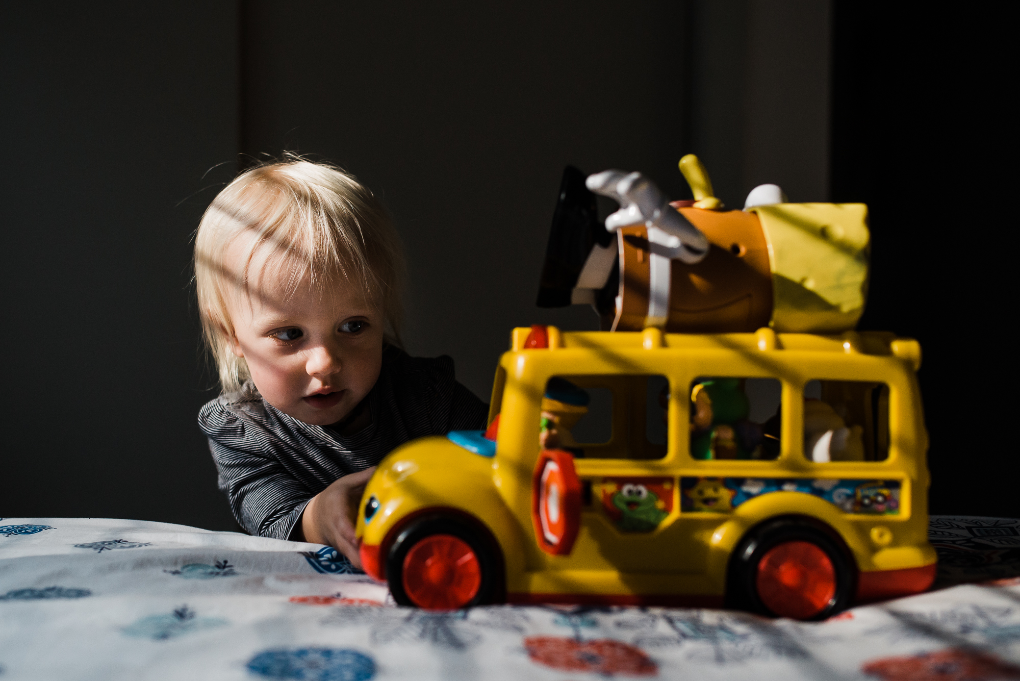 child with toy bus in dramatic light - Documentary Family Photography