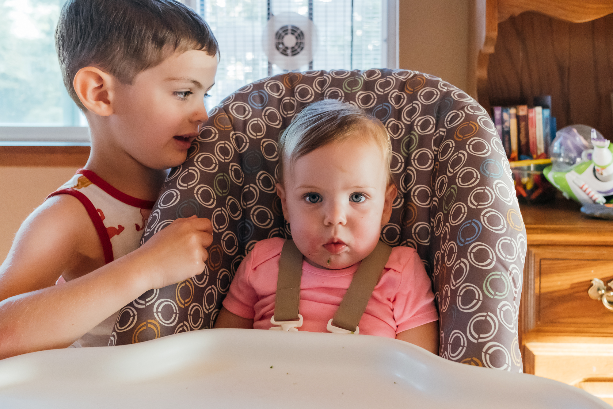 baby in high chair ignores older brother - Documentary Family Photography